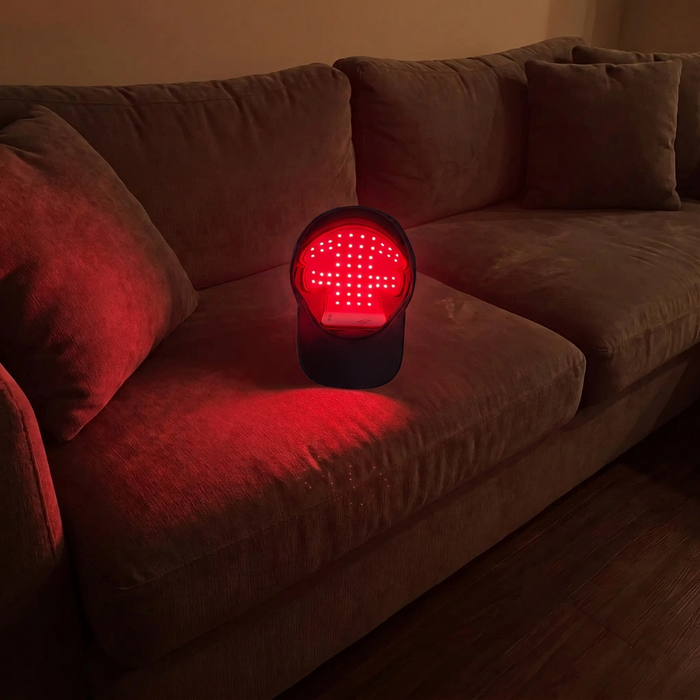 Optimal red light therapy cap glowing on a sofa